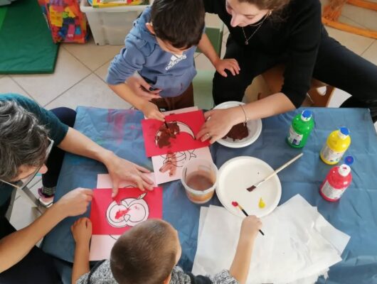 Due bambini che dipingono, visti dall'alto, insieme a due educatrici adulte