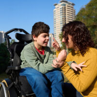 Bambino disabile sulla sedia a rotelle all'aperto insieme ai genitori